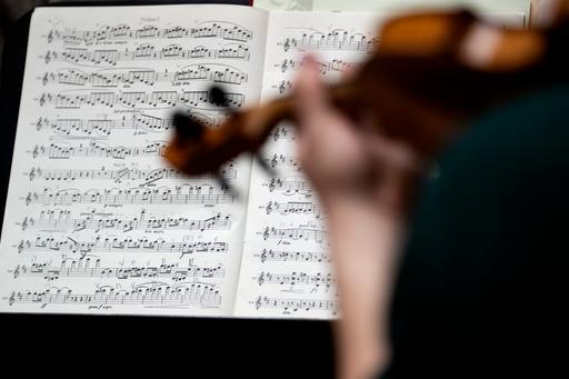 Hand holding a violin. Sheet music in the background.