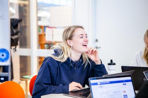 A smiling student sits at a table with a laptop.